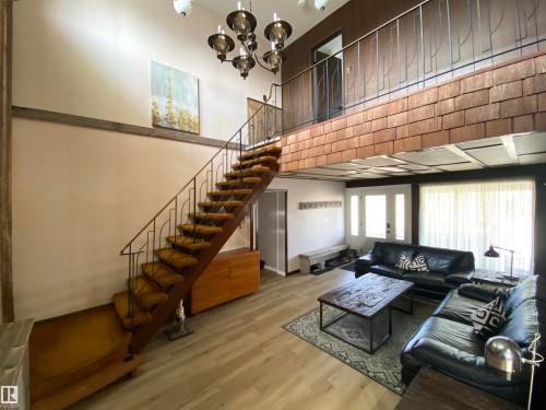 Open concept living area featuring light wood-finish flooring, a grand staircase with decorative railing, a second-story overlook with wood shingle siding, and a double-door entry with sidelights - 12137 50 Street, Edmonton, AB - Indoor Photo Showing Other Room