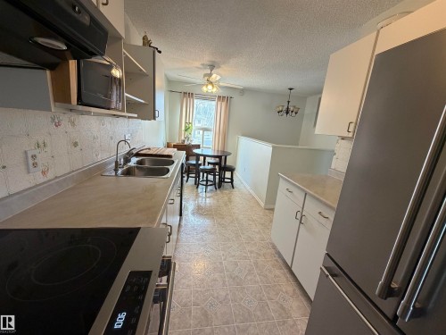 Kitchen featuring tile flooring, a dual basin stainless steel sink, built-in electric cooktop, white cabinetry, and light-toned countertops - 1875 Mill Woods Road E, Edmonton, AB - Indoor Photo Showing Kitchen With Double Sink