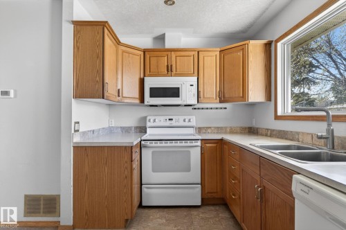 Kitchen featuring wood-finish cabinetry, light-toned countertops, and a double basin sink with a modern faucet - 13412 108 Street, Edmonton, AB - Indoor Photo Showing Kitchen With Double Sink