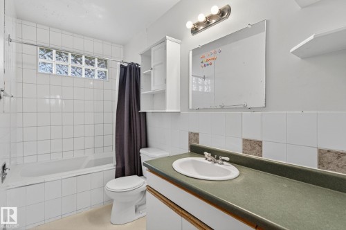 Bathroom with a white tiled shower/tub combination, glass block window, and a white vanity featuring an integrated sink, green countertop, and a wall-mounted light fixture above the mirror - 13412 108 Street, Edmonton, AB - Indoor Photo Showing Bathroom
