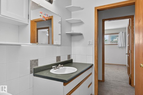 Bathroom vanity featuring a white drop-in sink with chrome fixtures, set into a dark countertop, against a tiled wall - 13412 108 Street, Edmonton, AB - Indoor Photo Showing Bathroom