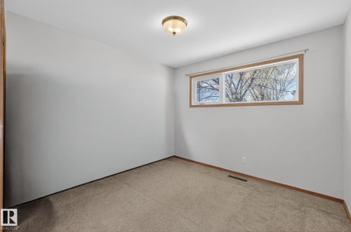 Carpeted interior space featuring a single window with wood-finish trim, light gray walls, and a flush mount ceiling fixture - 13412 108 Street, Edmonton, AB - Indoor Photo Showing Other Room