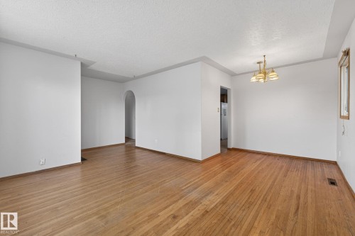 Spacious room featuring wood-finish flooring, white walls, an arched entryway, and a brass-tone chandelier - 13412 108 Street, Edmonton, AB - Indoor Photo Showing Other Room