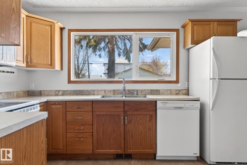 Kitchen featuring wood cabinetry, laminate countertops, a dual-basin stainless steel sink, and a white dishwasher - 13412 108 Street, Edmonton, AB - Indoor Photo Showing Kitchen With Double Sink