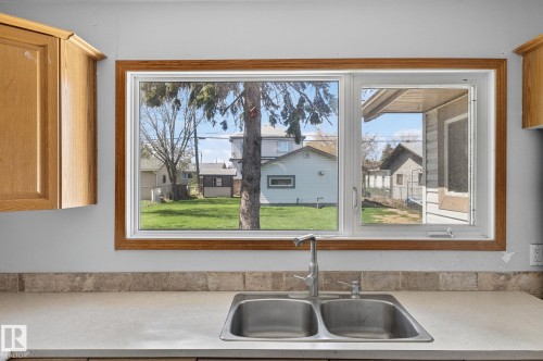 Dual stainless steel sink with a single-handle faucet, set within a light-toned countertop and a natural stone tile backsplash - 13412 108 Street, Edmonton, AB - Indoor Photo Showing Kitchen With Double Sink
