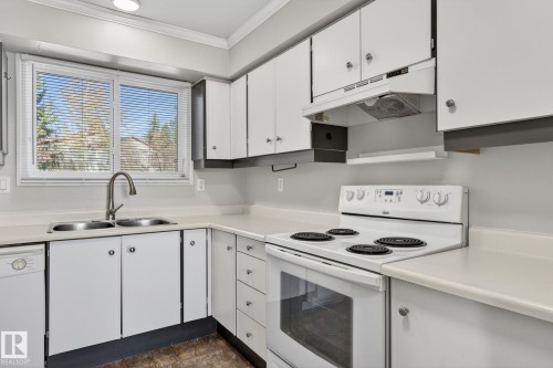 Bright kitchen featuring white cabinetry, a dual basin stainless steel sink with a gooseneck faucet, light-toned countertops, a white electric range, and a white dishwasher - 18 17409 95 Street, Edmonton, AB - Indoor Photo Showing Kitchen With Double Sink