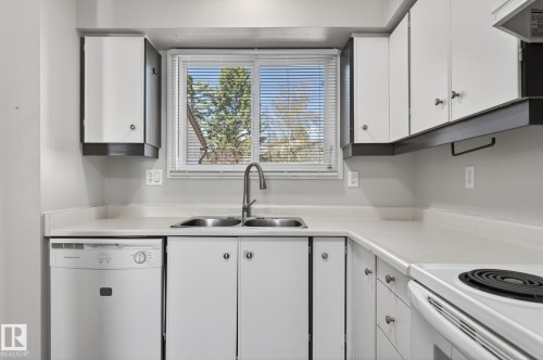 Kitchen featuring white cabinetry with dark accents, a double basin stainless steel sink, a modern gooseneck faucet, light-toned countertops, and an integrated dishwasher - 18 17409 95 Street, Edmonton, AB - Indoor Photo Showing Kitchen With Double Sink