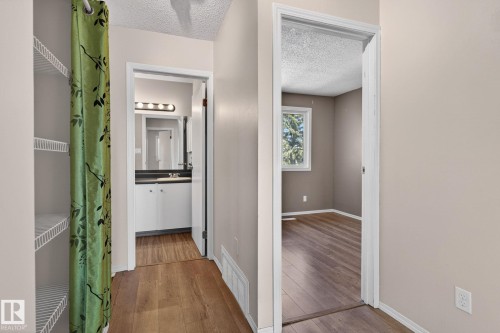 Hallway featuring wood-finish flooring, neutral wall paint, and two open doorways - 18 17409 95 Street, Edmonton, AB - Indoor