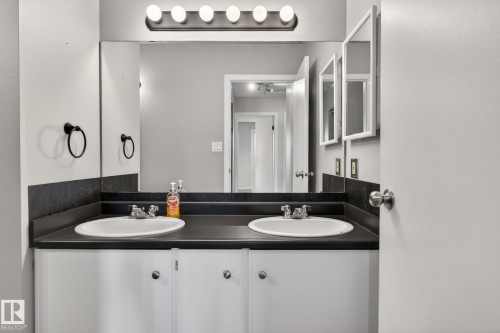 Double vanity featuring integrated sinks, dark countertop, and white cabinetry - 18 17409 95 Street, Edmonton, AB - Indoor Photo Showing Bathroom