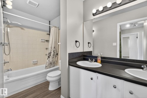 Bathroom featuring a dual-sink vanity with white cabinetry and a dark countertop, an integrated wall mirror, and a tub-shower combination with tiled surround and overhead lighting - 18 17409 95 Street, Edmonton, AB - Indoor Photo Showing Bathroom