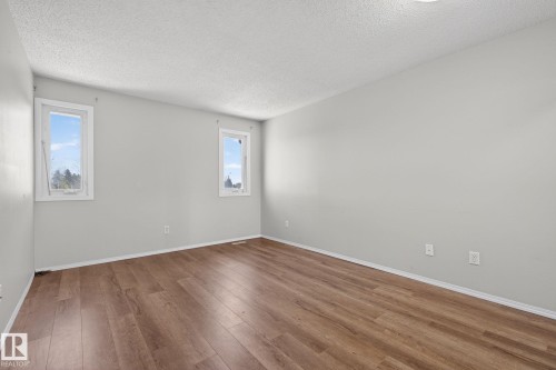 Spacious room featuring wood-finish flooring, light grey walls, white trim, and two double-hung windows - 18 17409 95 Street, Edmonton, AB - Indoor Photo Showing Other Room