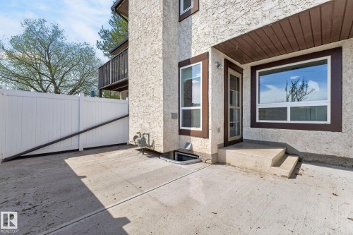 Rear patio featuring concrete surfacing, a white privacy fence, and a basement window well - 18 17409 95 Street, Edmonton, AB - Outdoor With Exterior