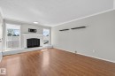 Living area featuring wood-finish flooring, a white fireplace with a dark grate, and dual windows - 18 17409 95 Street, Edmonton, AB  - Indoor Photo Showing Living Room With Fireplace 