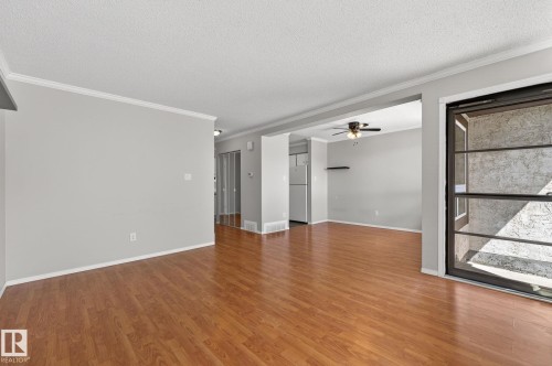 Spacious living area featuring wood-finish flooring, light gray wall paint, and white crown molding - 18 17409 95 Street, Edmonton, AB - Indoor Photo Showing Other Room