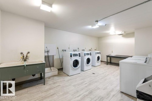 Dedicated laundry facility featuring multiple washing machines, dryers & a utility sink. - 101 8604 Gateway Boulevard, Edmonton, AB - Indoor Photo Showing Laundry Room