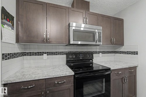 Kitchen featuring dark wood-finish cabinetry, light-toned countertops, a black electric range, and a stainless steel over-the-range microwave - 1211 29 Street, Edmonton, AB - Indoor Photo Showing Kitchen