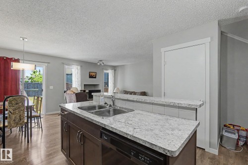 Kitchen island featuring a double basin stainless steel sink, dark wood-finish cabinetry, a built-in dishwasher, and granite-style countertops - 1211 29 Street, Edmonton, AB - Indoor Photo Showing Kitchen With Double Sink