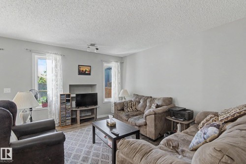 Living area featuring light gray walls, a textured ceiling, two windows with white trim, and a recessed alcove - 1211 29 Street, Edmonton, AB - Indoor Photo Showing Living Room