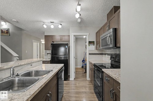 Kitchen featuring wood-finish flooring, dark cabinetry, and light-toned countertops - 1211 29 Street, Edmonton, AB - Indoor Photo Showing Kitchen With Double Sink