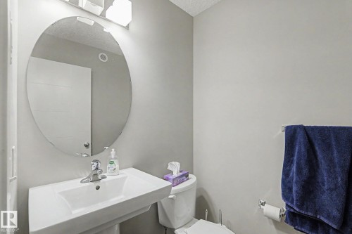 Pedestal sink with a polished chrome faucet, an oval mirror, and a wall-mounted vanity light fixture - 1211 29 Street, Edmonton, AB - Indoor Photo Showing Bathroom