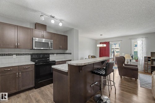 Kitchen featuring wood-finish flooring, dark wood cabinetry, stainless steel microwave, black electric range, and light-toned countertops - 1211 29 Street, Edmonton, AB - Indoor Photo Showing Kitchen