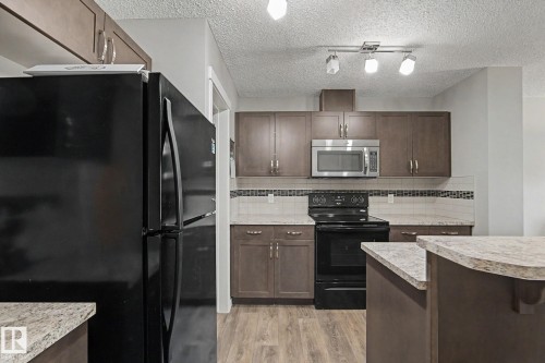 Contemporary kitchen featuring wood-finish flooring, dark wood cabinetry, light stone-finish countertops, and a decorative tile backsplash - 1211 29 Street, Edmonton, AB - Indoor Photo Showing Kitchen