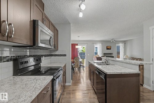 Kitchen featuring wood-finish cabinetry, stainless steel appliances, a tile backsplash with mosaic accent, light-toned countertops, and wood-finish flooring - 1211 29 Street, Edmonton, AB - Indoor Photo Showing Kitchen With Double Sink With Upgraded Kitchen