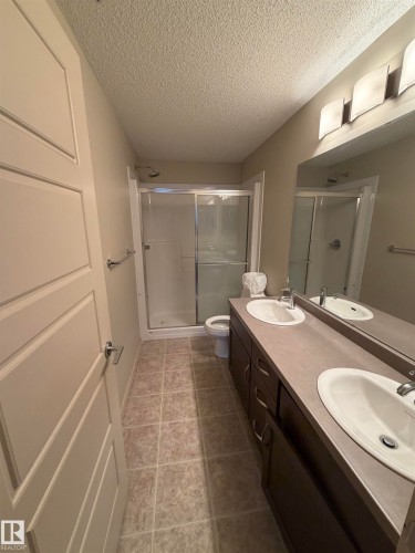 Well-appointed bathroom featuring a double vanity with two sinks, a large mirror, and an enclosed shower - 313 6084 Stanton Drive, Edmonton, AB - Indoor Photo Showing Bathroom