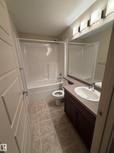 Well-maintained bathroom featuring a vanity with an integrated sink and countertop, a toilet, and a combination bathtub and shower with a white surround - 313 6084 Stanton Drive, Edmonton, AB - Indoor Photo Showing Bathroom