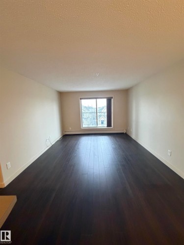 The main living area features dark wood flooring, light-colored walls, and a window providing natural light - 313 6084 Stanton Drive, Edmonton, AB - Indoor Photo Showing Other Room