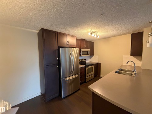 The kitchen features dark wood cabinetry, stainless steel appliances, and a double basin sink - 313 6084 Stanton Drive, Edmonton, AB - Indoor Photo Showing Kitchen With Double Sink