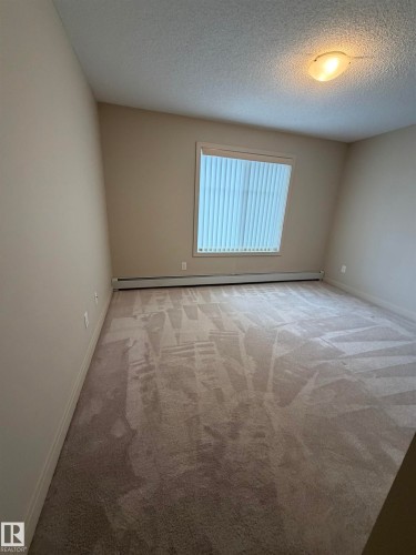 Room featuring neutral-toned walls, textured ceiling, a flush mount light fixture, and wall-to-wall carpeting - 313 6084 Stanton Drive, Edmonton, AB - Indoor Photo Showing Other Room