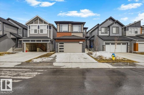 Contemporary two-story residence featuring a two-car garage with a modern glass-panel door, mixed-material facade with wood-look siding and stone accents, and a paved driveway - 7056 182 Avenue, Edmonton, AB - Outdoor With Facade