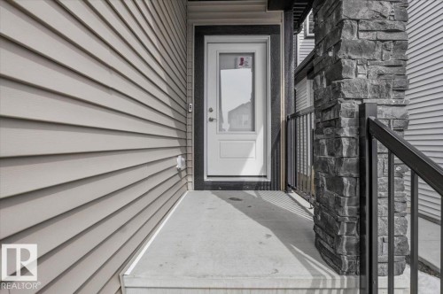 Entryway featuring stacked stone column, metal railing, concrete porch, white door with dark trim, and horizontal siding - 7056 182 Avenue, Edmonton, AB - Outdoor With Exterior