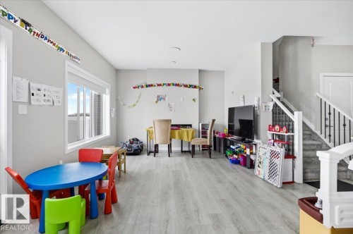 Open-concept living space featuring wood-finish flooring, a large window, light gray wall tones, and a staircase with black metal balusters - 7056 182 Avenue, Edmonton, AB - Indoor