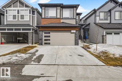 Modern two-story residence featuring a neutral exterior palette, stone veneer accents, wood-look siding, and a contemporary garage door with horizontal frosted glass inserts - 7056 182 Avenue, Edmonton, AB - Outdoor With Facade