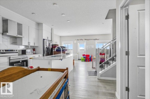 Open-concept kitchen featuring white cabinetry, stainless steel appliances, a large island with sink, light-toned flooring, and recessed lighting - 7056 182 Avenue, Edmonton, AB - Indoor Photo Showing Other Room
