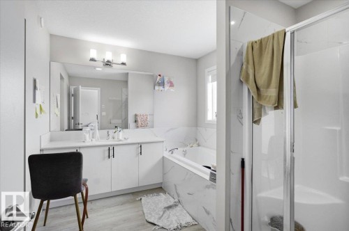Full bathroom featuring a glass-enclosed shower, a large soaking tub with a tiled surround, a vanity with a white countertop and base cabinetry, a wide mirror, and a window - 7056 182 Avenue, Edmonton, AB - Indoor Photo Showing Bathroom