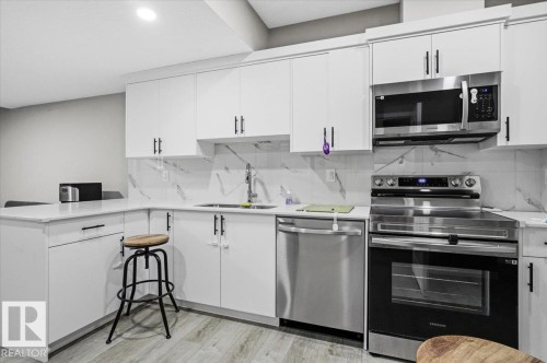 Contemporary kitchen featuring white cabinetry with matte black hardware, stainless steel appliances, a white countertop, and a marble-patterned backsplash - 7056 182 Avenue, Edmonton, AB - Indoor Photo Showing Kitchen