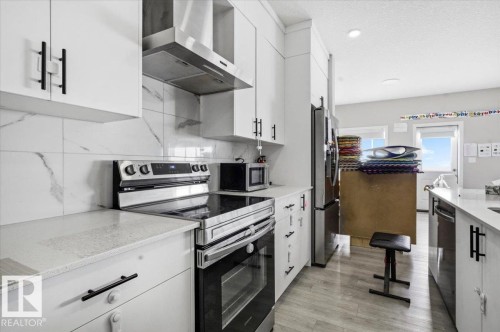 Modern kitchen featuring light wood-finish flooring, white cabinetry with contemporary black hardware, white countertops, and a white tile backsplash with gray veining - 7056 182 Avenue, Edmonton, AB - Indoor Photo Showing Kitchen With Upgraded Kitchen