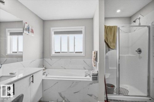 Bathroom featuring a built-in tub with tile surround, a separate shower with glass enclosure, a vanity with a light-colored countertop, and a window with blinds - 7056 182 Avenue, Edmonton, AB - Indoor Photo Showing Bathroom