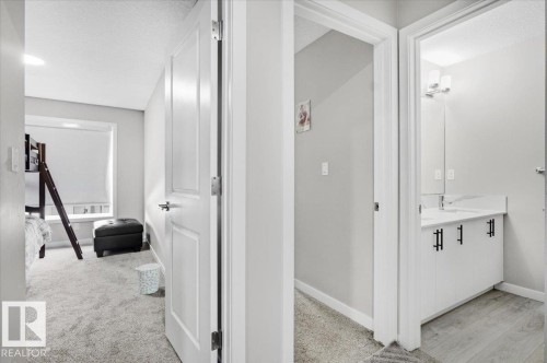 White panel doors open to a carpeted room with a window and a bathroom featuring a white vanity with black hardware, a rectangular undermount sink, and light wood-finish flooring - 7056 182 Avenue, Edmonton, AB - Indoor Photo Showing Other Room