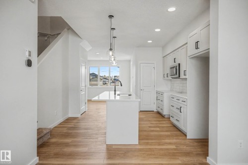 Kitchen featuring wood-finish flooring, recessed lighting, a central island with a sink, pendant light fixtures, and white cabinetry with dark hardware - 720 Southfork Drive, Leduc, AB - Indoor Photo Showing Kitchen