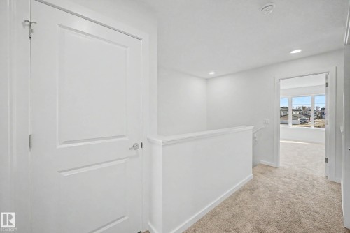 Carpeted hallway featuring a white paneled door with chrome hardware, white painted walls, recessed lighting, and a white half-wall railing - 720 Southfork Drive, Leduc, AB - Indoor Photo Showing Other Room
