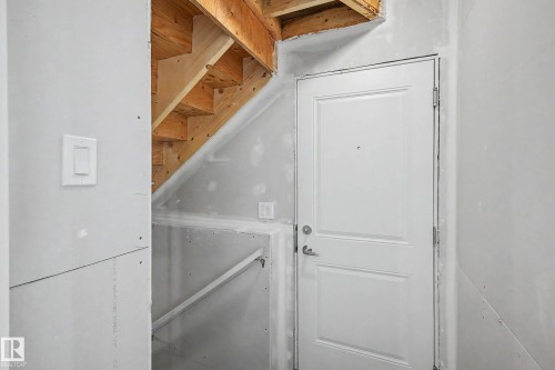 Unfinished interior space featuring exposed wood staircase framing, drywall installation, and a paneled white door with a lever handle - 720 Southfork Drive, Leduc, AB - Indoor Photo Showing Other Room