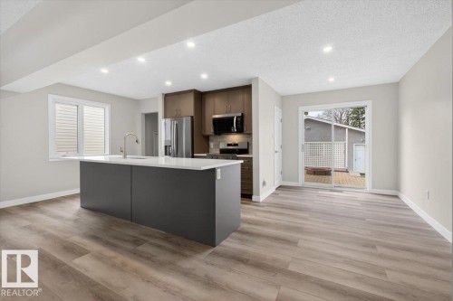 Open-concept kitchen featuring a dark gray island with a white countertop, stainless steel appliances, recessed lighting, and wood-finish flooring - 9723 65 Avenue, Edmonton, AB - Indoor Photo Showing Kitchen With Upgraded Kitchen