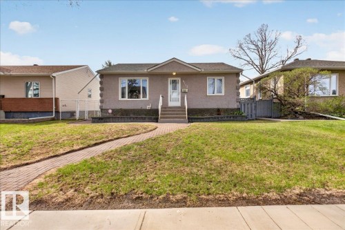 Stucco facade residence featuring a front entry porch with white railings, a curved brick paver walkway, a landscaped front yard with a low retaining wall, and a shingled roof - 9723 65 Avenue, Edmonton, AB - Outdoor