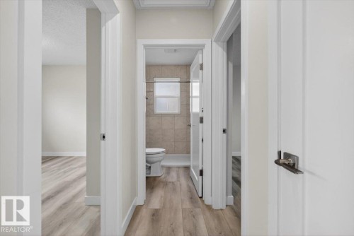 Hallway featuring light wood-finish flooring, white paneled doors, and contemporary door hardware - 9723 65 Avenue, Edmonton, AB - Indoor