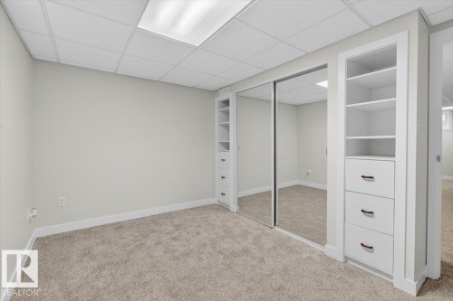 Carpeted room featuring a drop ceiling with integrated lighting, mirrored sliding closet doors, and built-in shelving units with drawers - 9723 65 Avenue, Edmonton, AB - Indoor Photo Showing Other Room