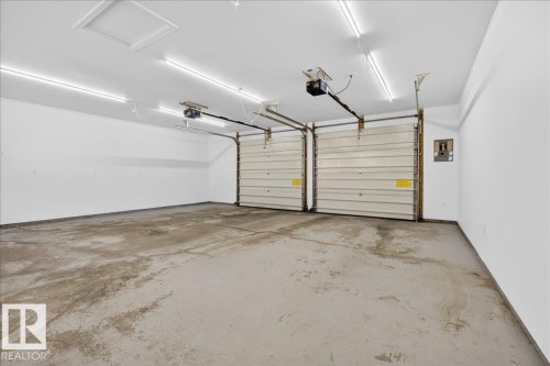 Two-car garage featuring segmented overhead doors with openers, exposed ceiling joists, and fluorescent strip lighting - 9723 65 Avenue, Edmonton, AB - Indoor Photo Showing Garage
